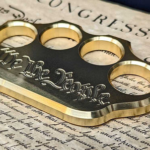 brass knuckles engraved with “we the people” on top of Constitution
